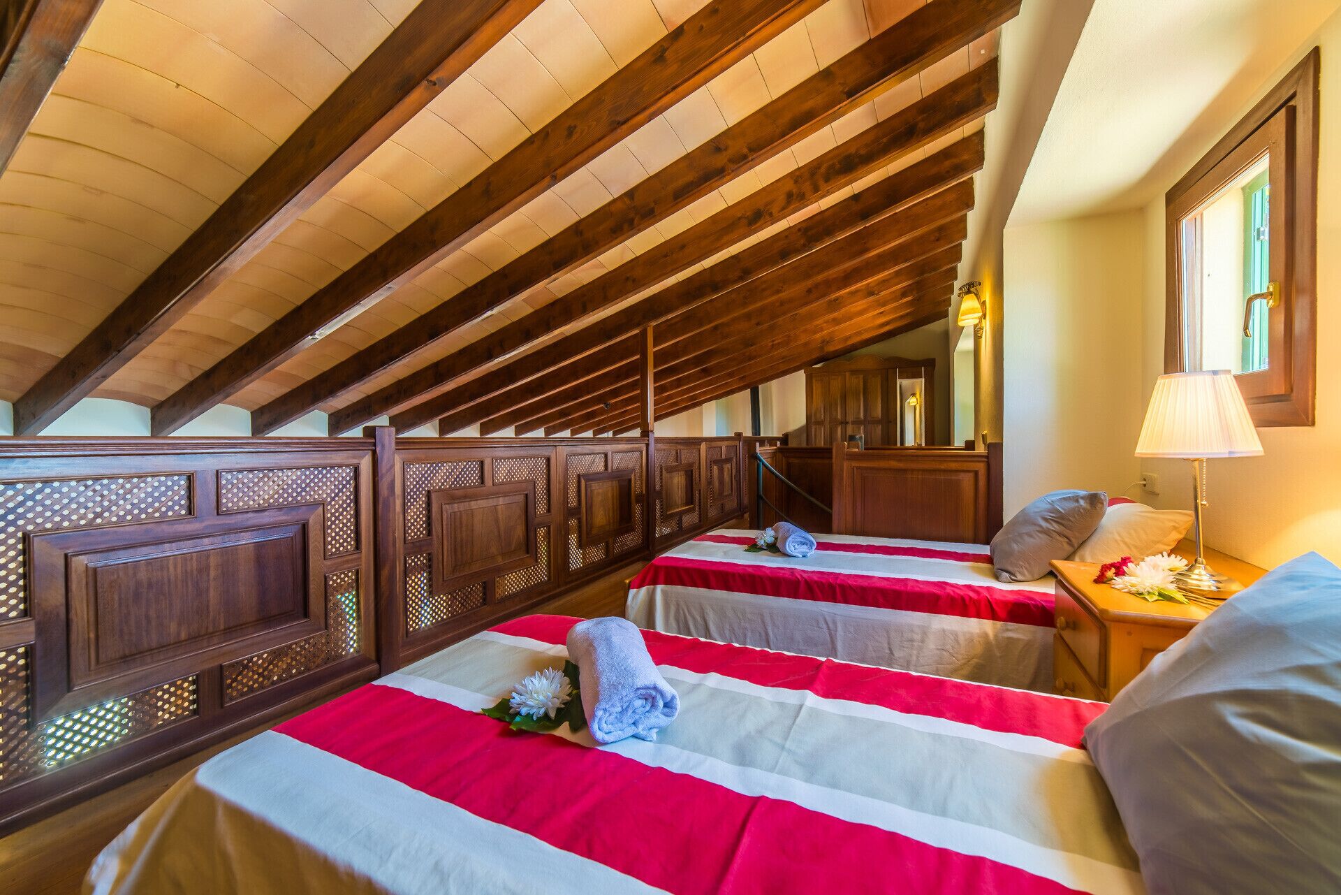 Une chambre d’hôtel avec deux lits, des poutres en bois au plafond, une fenêtre et une table de chevet avec une lampe.