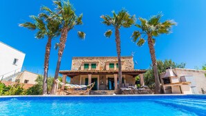A two-story building with a stone facade, a swimming pool in the foreground, and palm trees. - Maison près de la mer Goya avec piscine à Alcudia (Alcúdia)