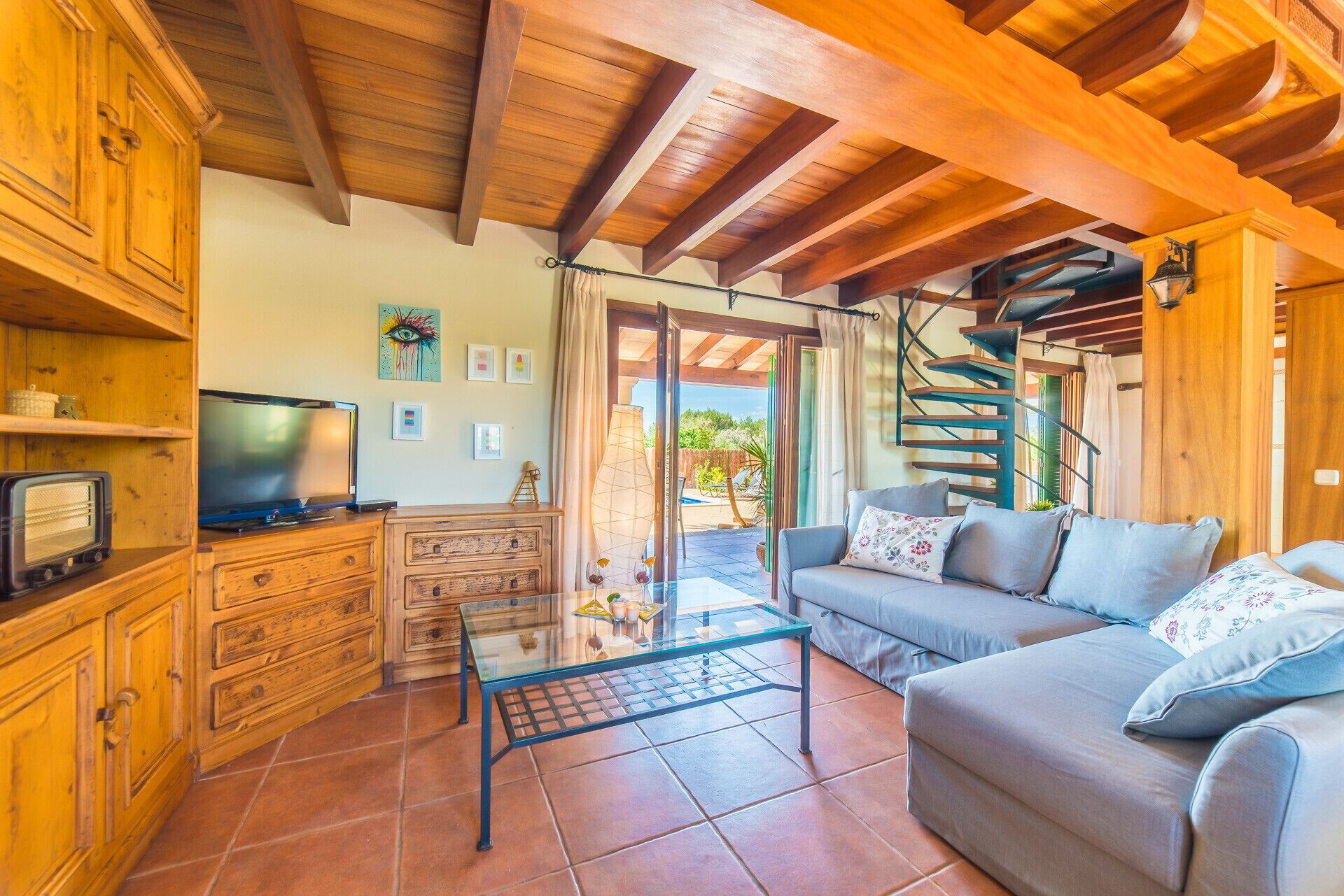 A cozy living room with a wooden ceiling, a television, a sofa, and a glass coffee table.