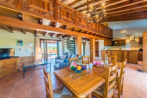 Relax in this open living area with a sofa, dining table, and TV, surrounded by natural light and a high ceiling.