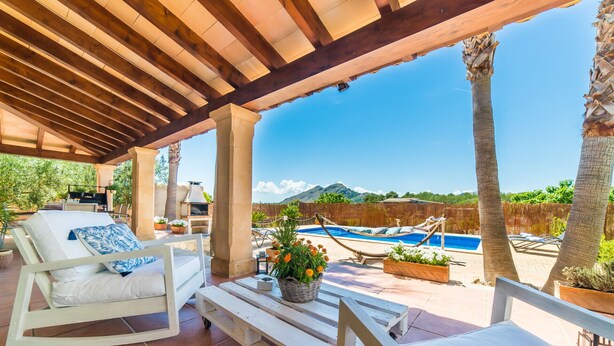 A covered outdoor area with a pool, white lounge chairs, and a view of mountains. - Maison près de la mer Goya avec piscine à Alcudia (Alcúdia)