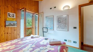 A room with a wooden ceiling, a bed with a floral bedspread, a radiator, and two framed maps on the wall. - Nice home in Champoluc (AO) with sauna (Champoluc (AO))