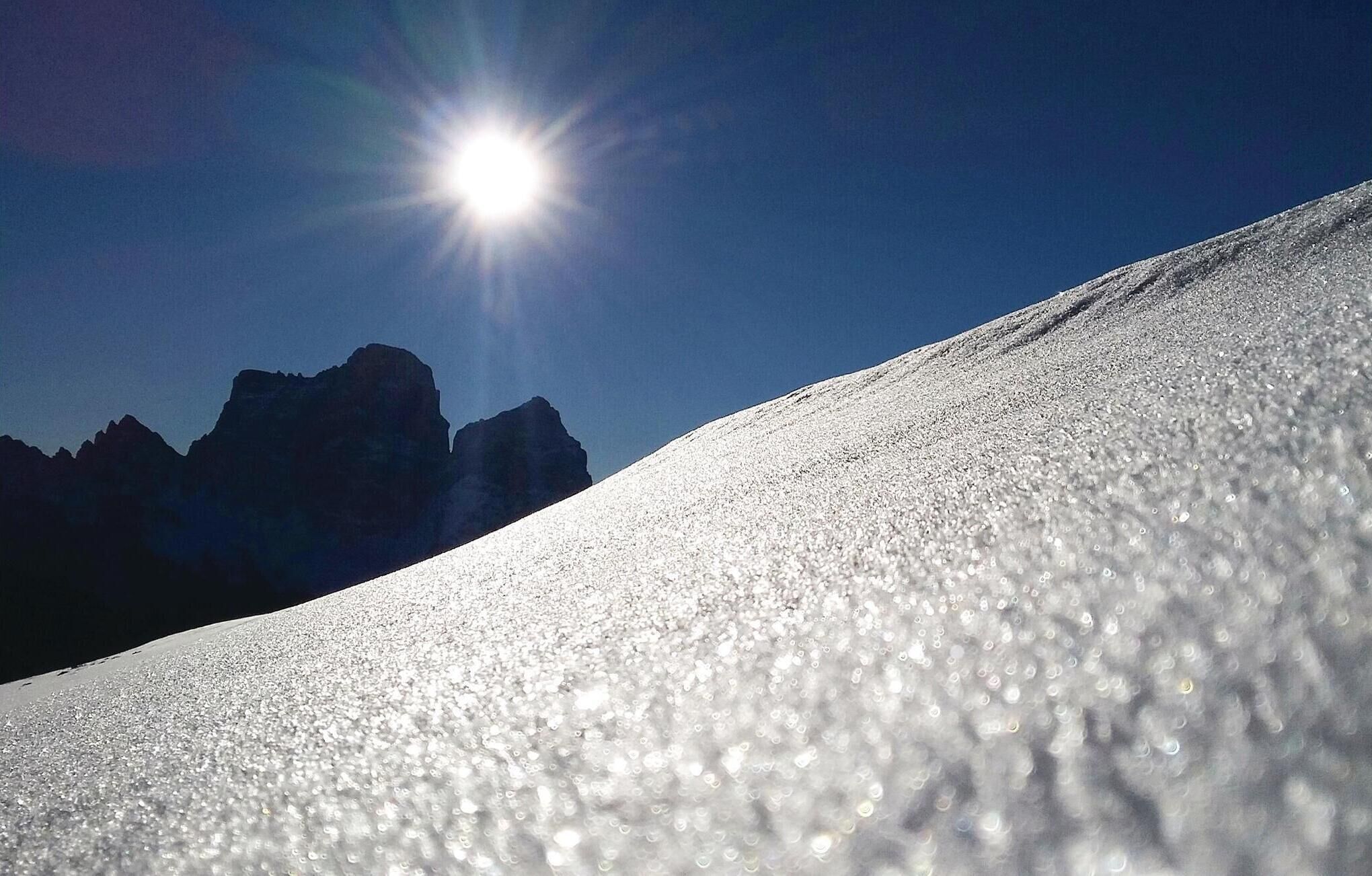 Pendio innevato con cielo sereno e montagne in lontananza.