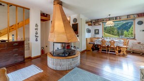 A cozy living room with a fireplace, wooden furniture, and a view of the outdoors. - Nice home in Champoluc (AO) with sauna (Champoluc (AO))