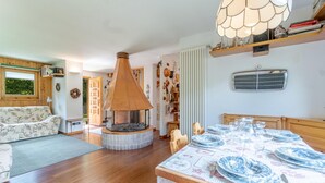 A cozy living room with a fireplace, wooden furniture, and a dining area with a table set for four. - Nice home in Champoluc (AO) with sauna (Champoluc (AO))