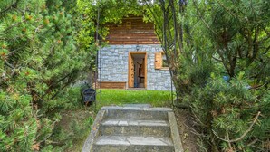 A stone cabin with a wooden door and a small porch, surrounded by dense pine trees. - Nice home in Champoluc (AO) with sauna (Champoluc (AO))
