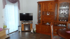 A living room with a flat-screen TV, wooden cabinet, and a dining table.