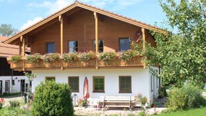 A two-story wooden building with a balcony, a bench, and a garden area. - Ferienhaus Gänseblümchen (Doppelhaushälfte) 65 qm (Höslwang)
