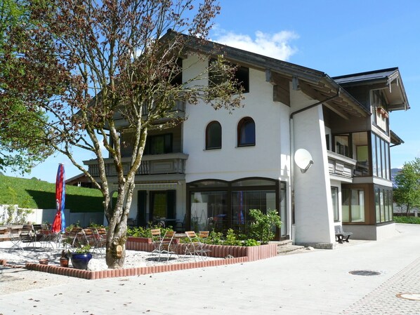 Un bâtiment à deux étages doté d’un balcon, de grandes fenêtres et d’un espace extérieur aménagé pour s’asseoir.