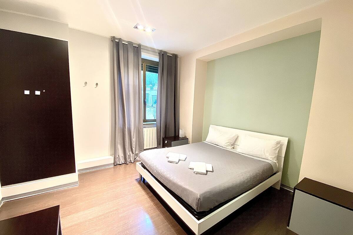 A modern hotel room with a large bed, a wardrobe, and a window with curtains.
