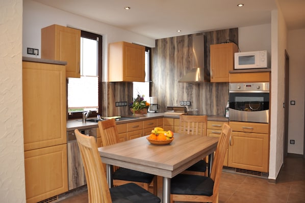 A modern kitchen with wooden cabinets, a stainless steel oven, a microwave, and a dining table with chairs.