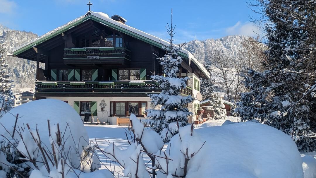 A traditional chalet with a wooden facade, balconies, and a snow-covered landscape.