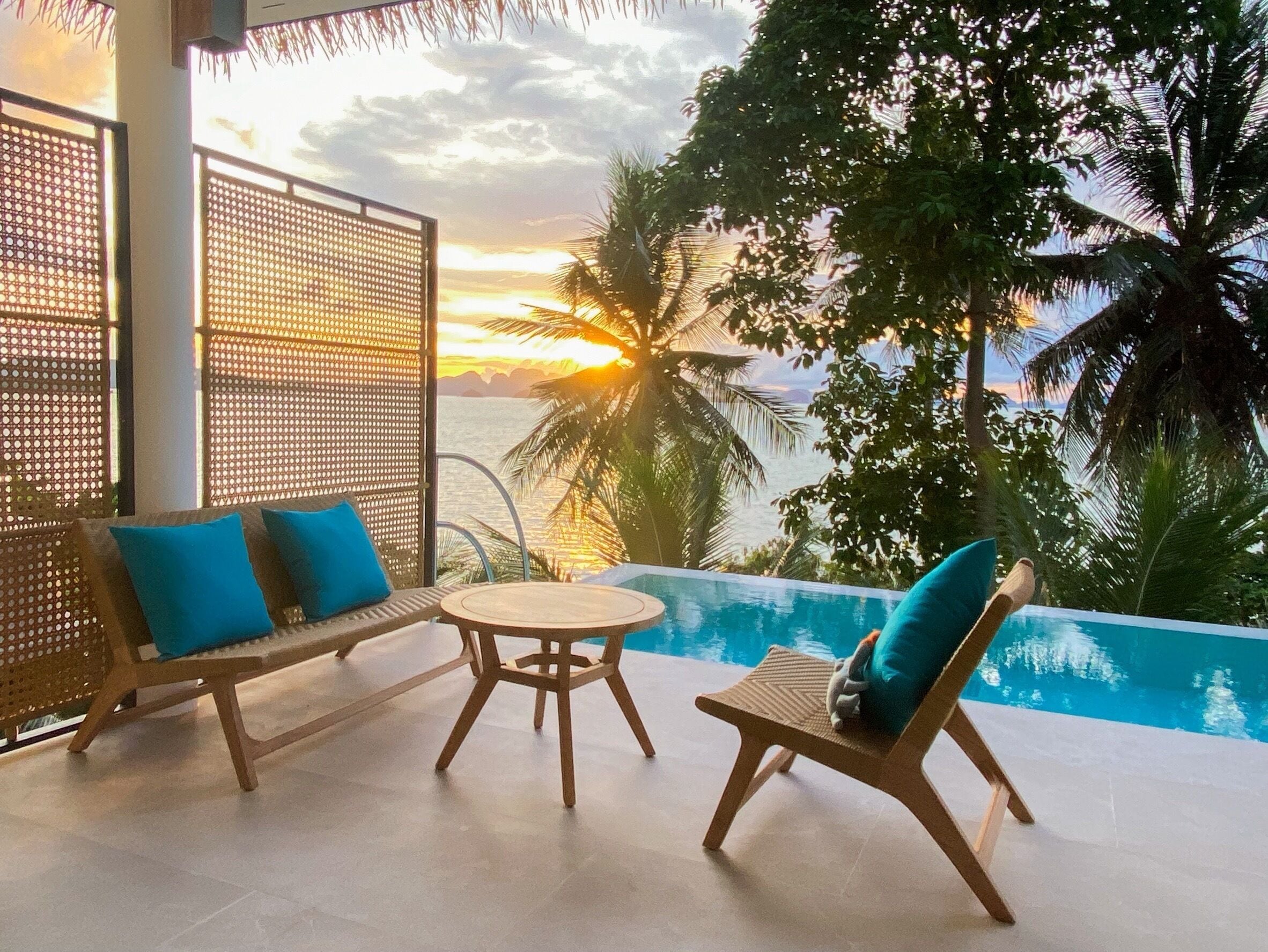 A poolside area with a wooden table and two lounge chairs, one with a blue cushion.