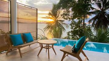 A poolside area with a wooden table and two lounge chairs, one with a blue cushion.