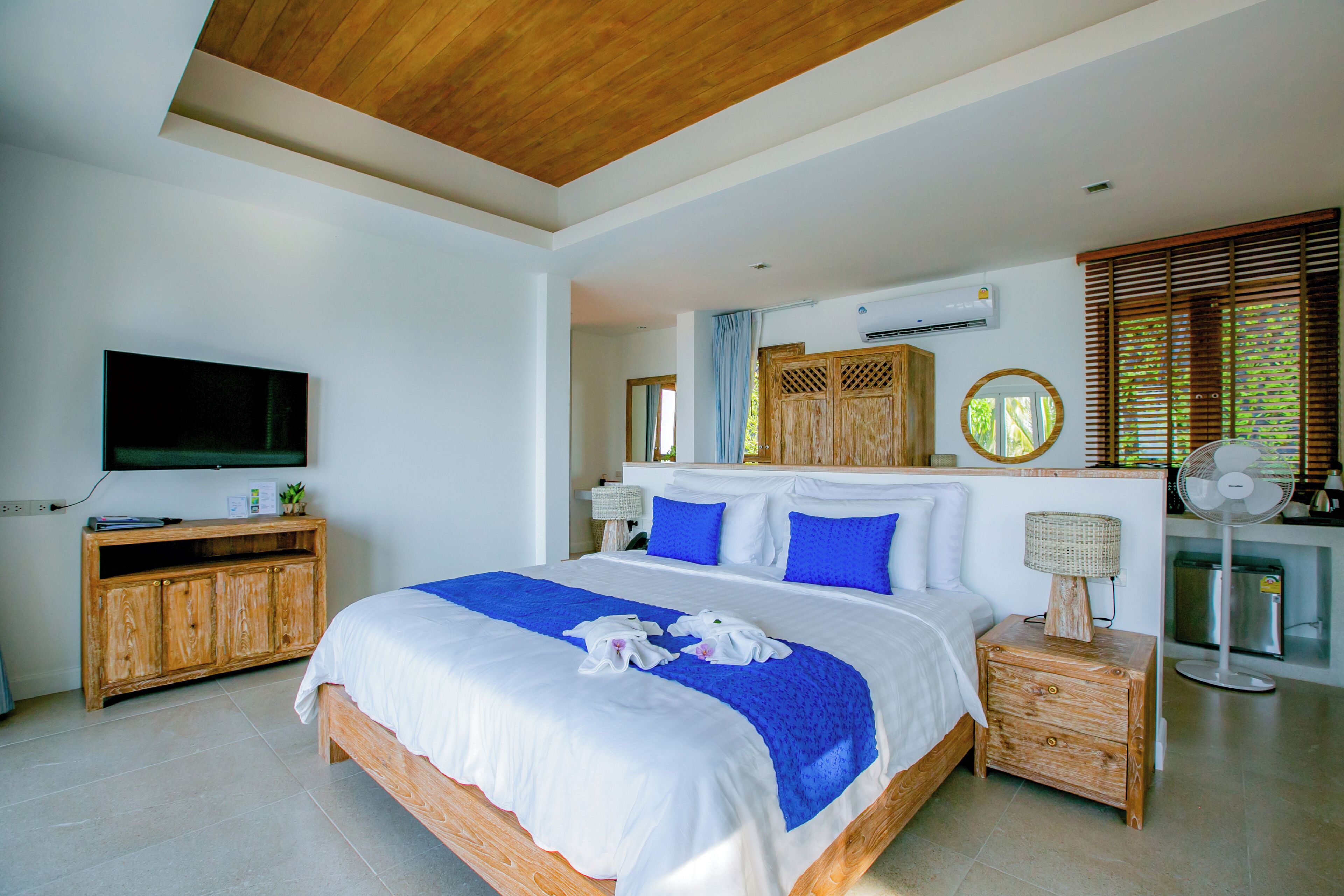 A modern bedroom with a large bed, wooden headboard, a flat-screen TV, a wooden cabinet, and a bedside table with a lamp.