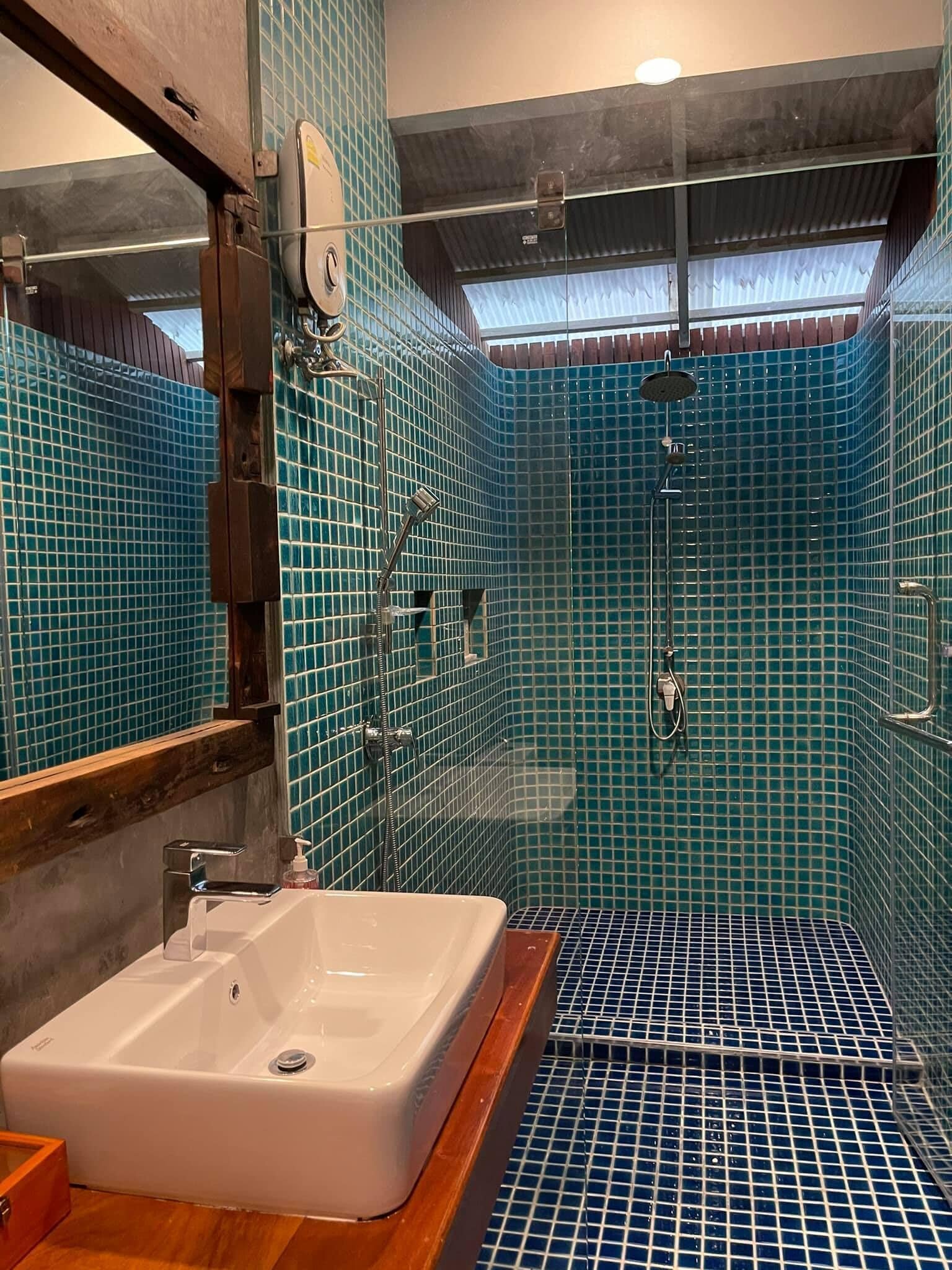 A bathroom with a white sink, a mirror, and a shower area with blue-tiled walls and floor.