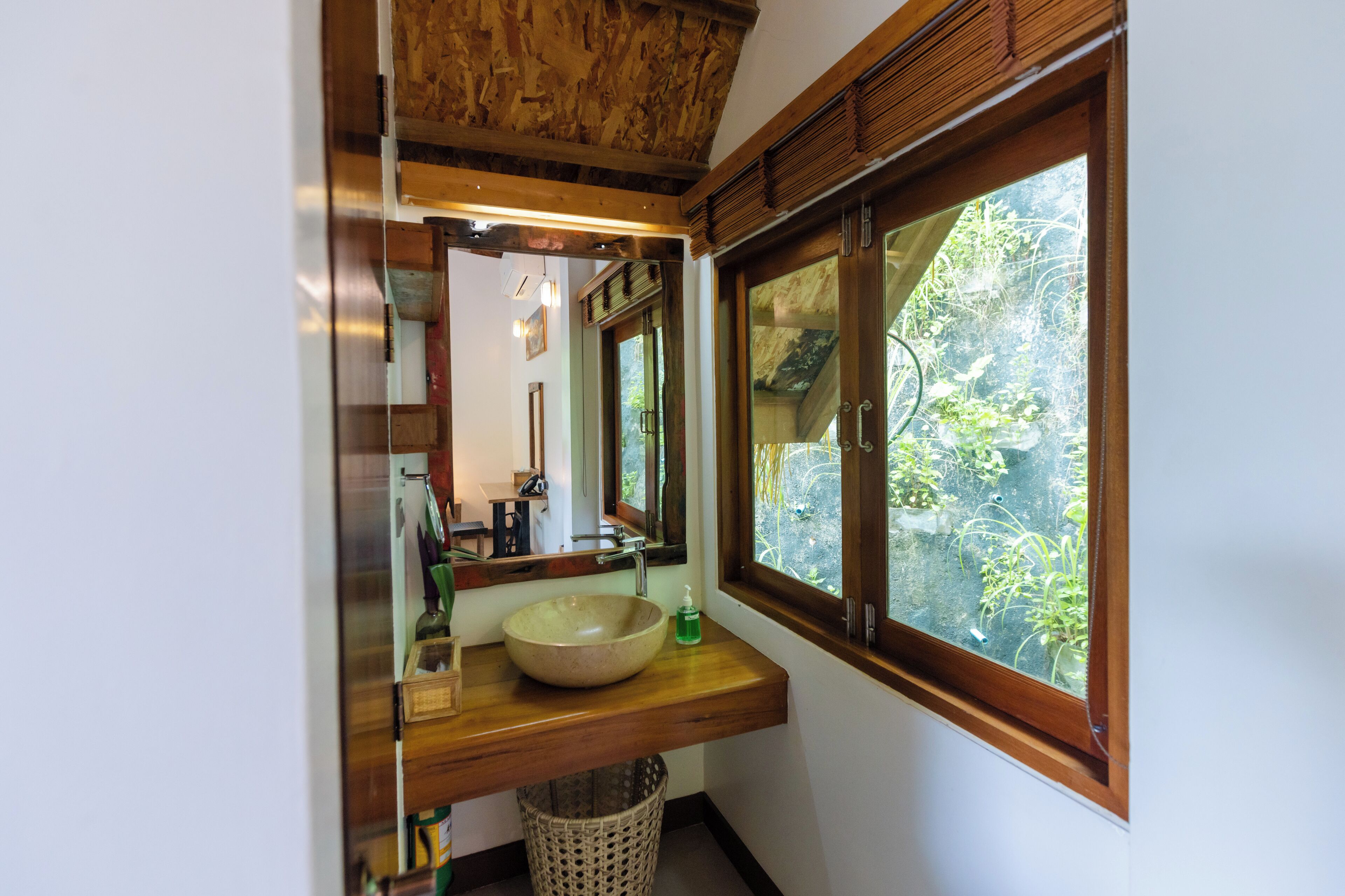 A bathroom with a wooden vanity, a large mirror, and a window with a view of greenery.