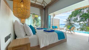 A bedroom with a large bed, a wooden nightstand, a hanging light fixture, and a view of the ocean.