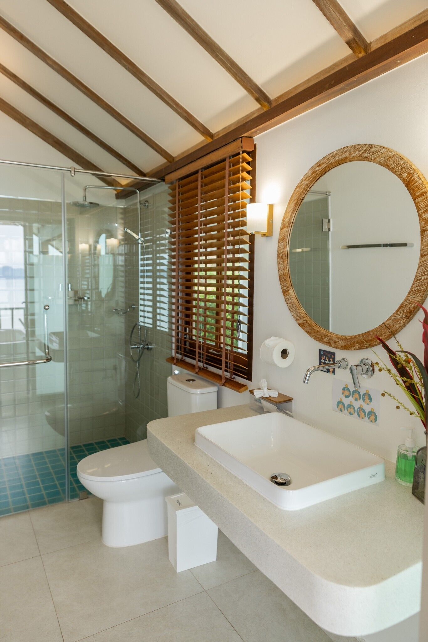 A modern bathroom with a glass-enclosed shower, a white toilet, a large sink, and a round mirror with a wooden frame.