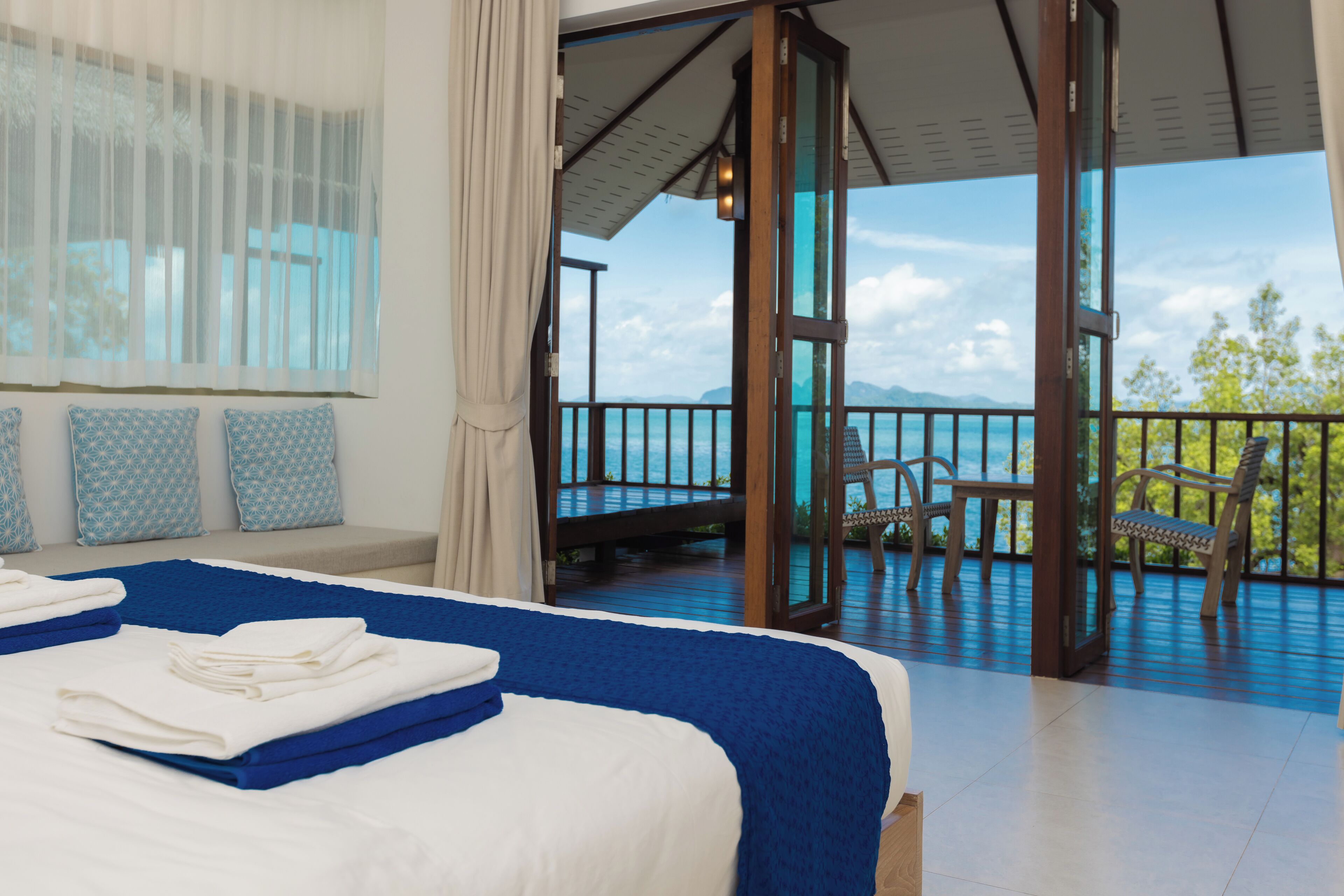 A hotel room with a large bed, a balcony with chairs, and a view of the sea.