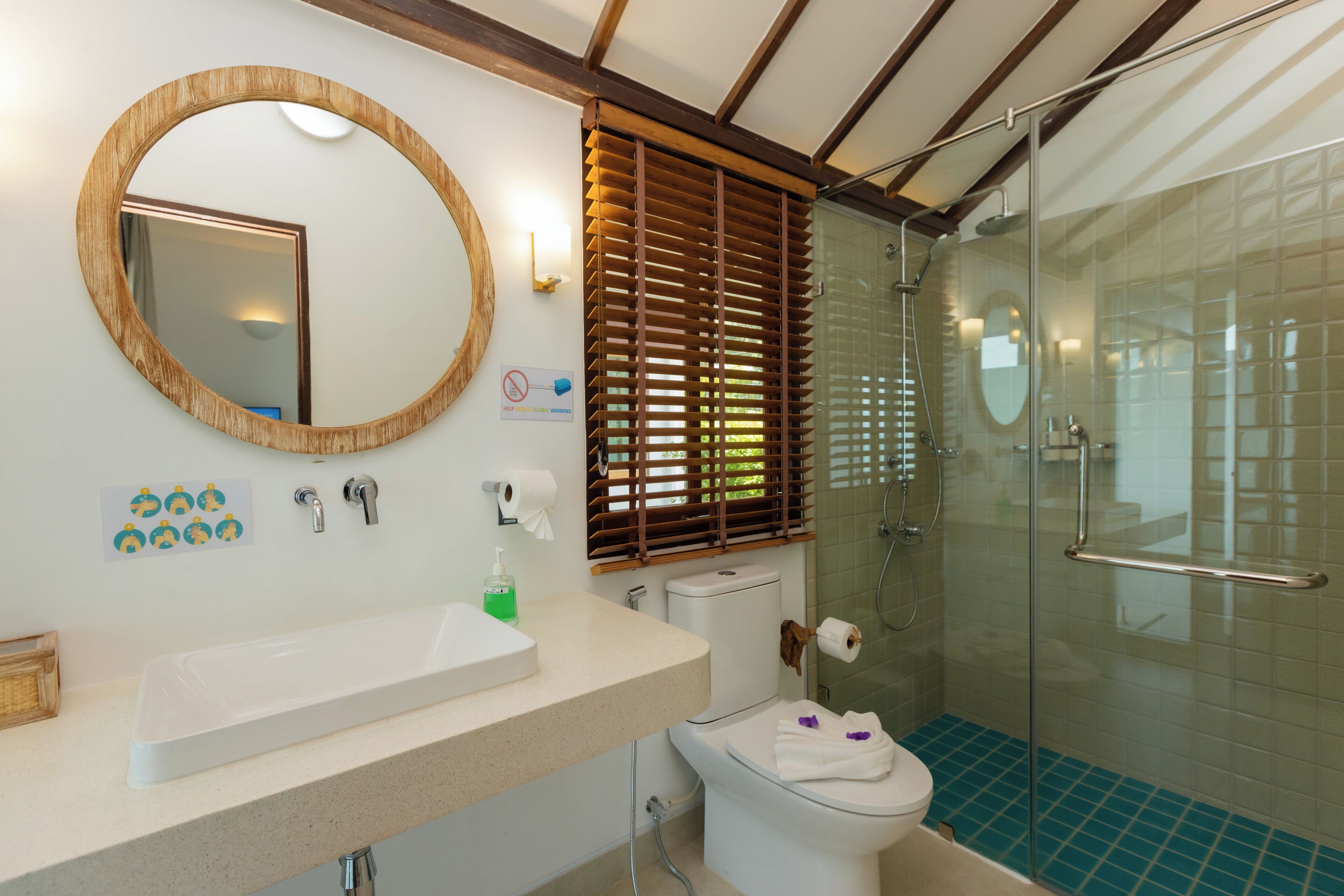 A bathroom with a white sink, a toilet, a glass shower enclosure, and wooden blinds.