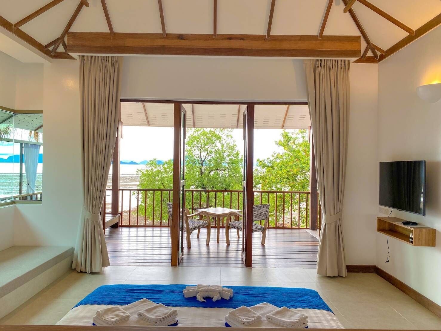 A room with a bed, a TV, and a balcony with a view of the sea.