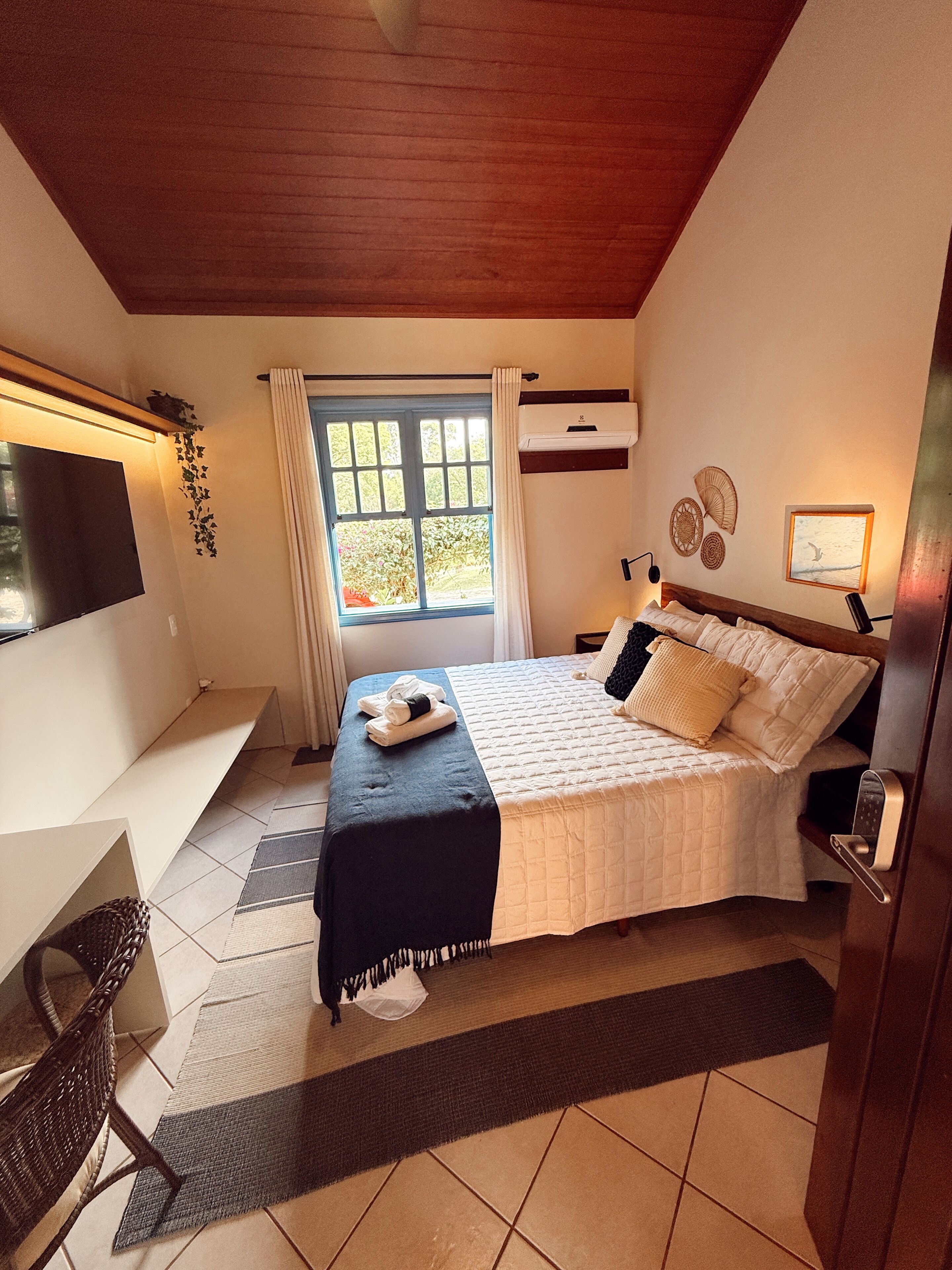 A bedroom with a bed, a desk, a chair, a window, and a TV.