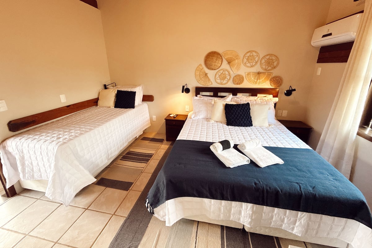 A hotel room with two beds, a wall-mounted air conditioner, and a decorative wall with woven items.