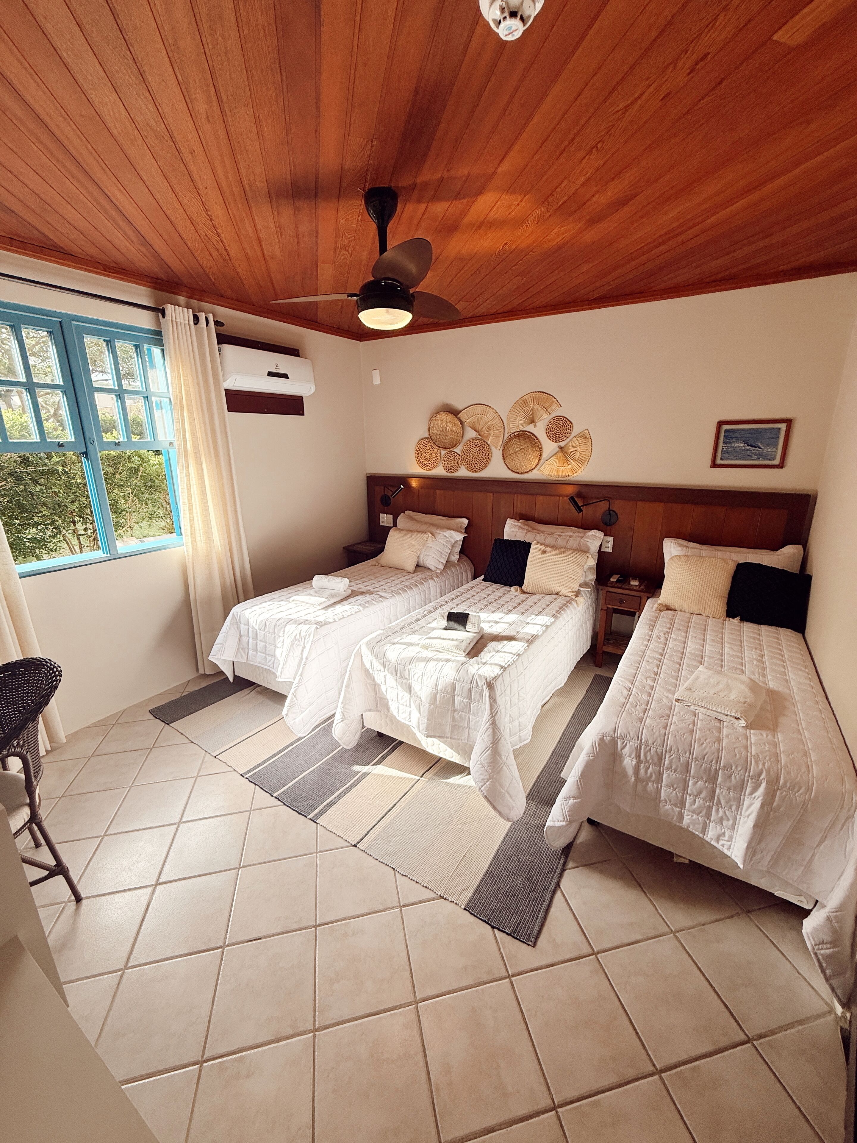 A room with two beds, a ceiling fan, a window with curtains, and a wall-mounted air conditioner.