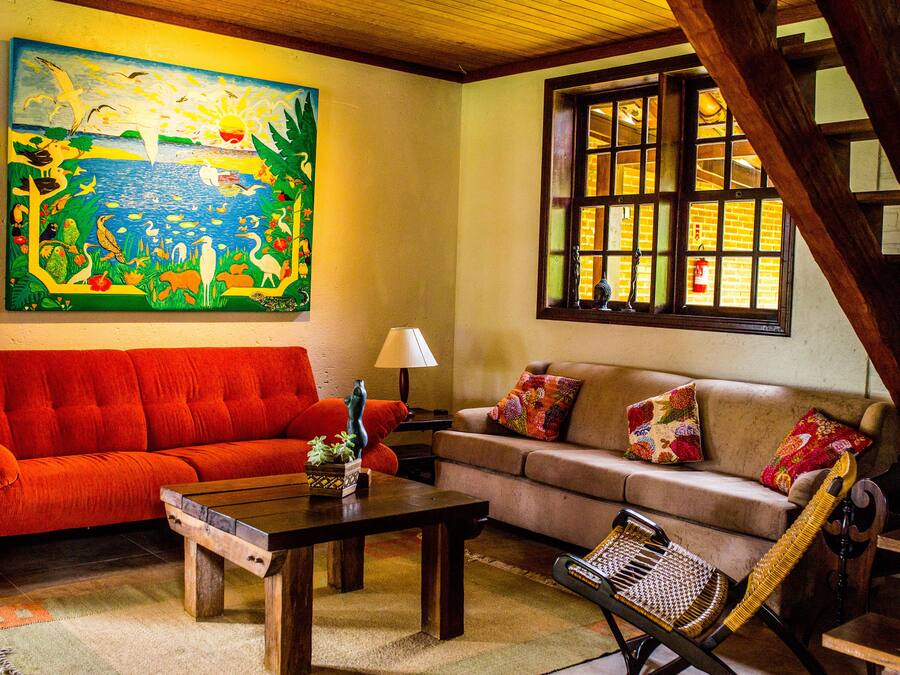 Ein Wohnzimmer mit einem roten Sofa, einem beigen Sofa, einem Holztisch, einem Korbstuhl und einem großen Gemälde an der Wand.