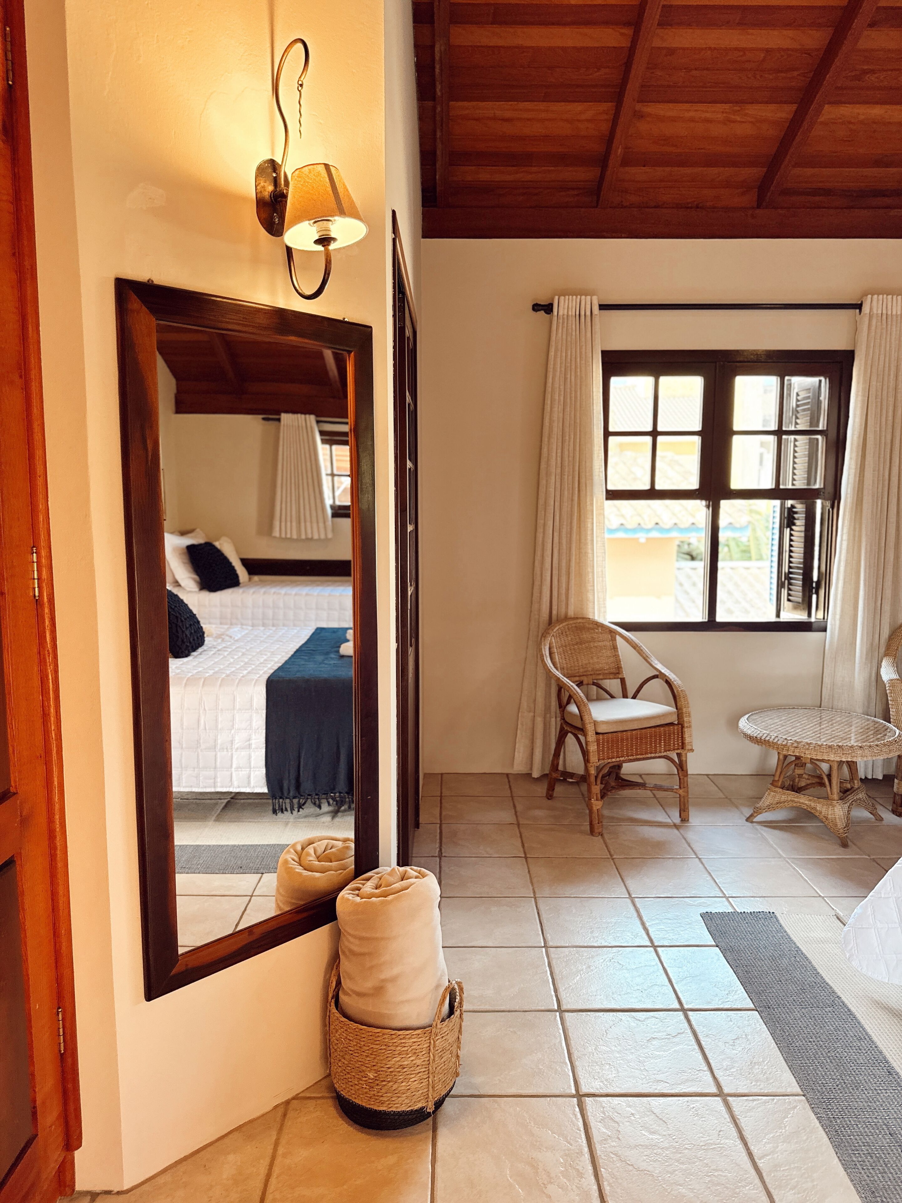 A room with a bed, a chair, a table, a mirror, and a window with curtains.
