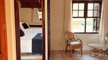 A room with a bed, a chair, a table, a mirror, and a window with curtains.