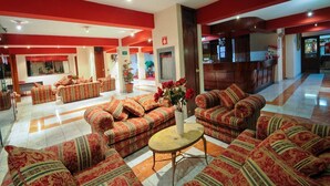 A spacious lobby with patterned sofas and a central coffee table, a reception desk, and a potted plant. - Qarmenqa Hotel (Cusco)
