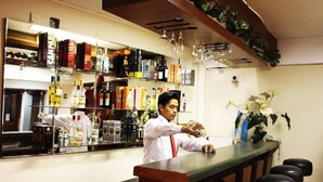 A bar area with a bartender preparing a drink, shelves stocked with various bottles, and a mirror reflecting the bar. - Qarmenqa Hotel (Cusco)