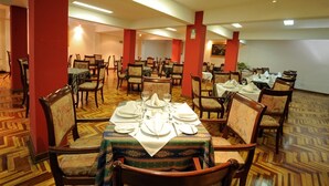 A dining area with multiple tables set for service, chairs arranged around them, and a patterned floor. - Qarmenqa Hotel (Cusco)