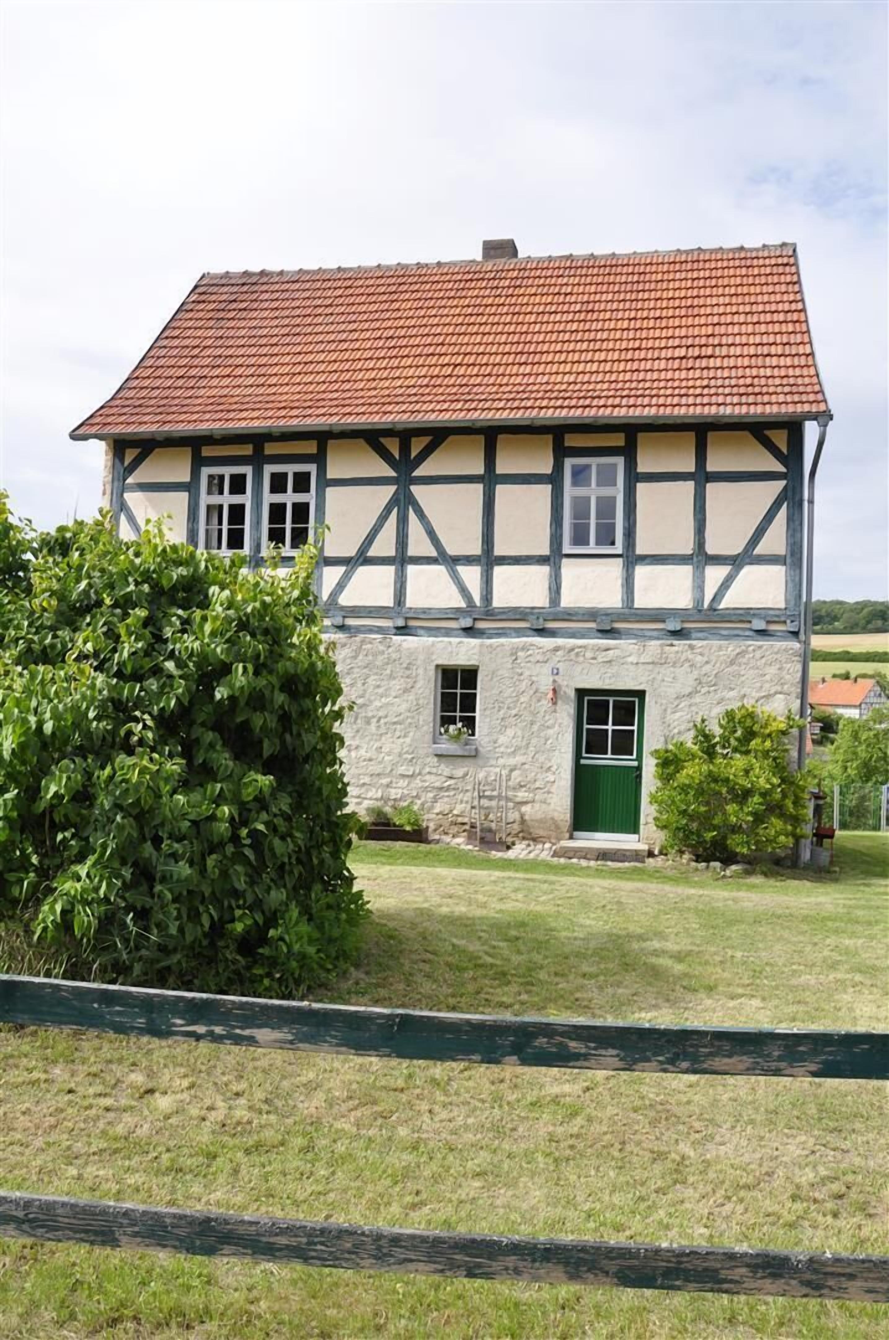 Ein traditionelles Fachwerkhäuschen mit rotem Ziegeldach, einer grünen Tür und einer Steinmauer.