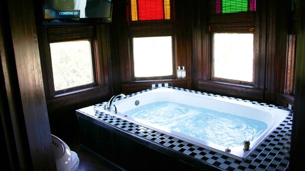 A large, rectangular bathtub with a checkered surround, positioned in a room with wooden paneled walls and windows.