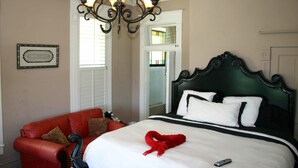 A hotel room with a large bed, a red leather sofa, a chandelier, and a framed picture on the wall.