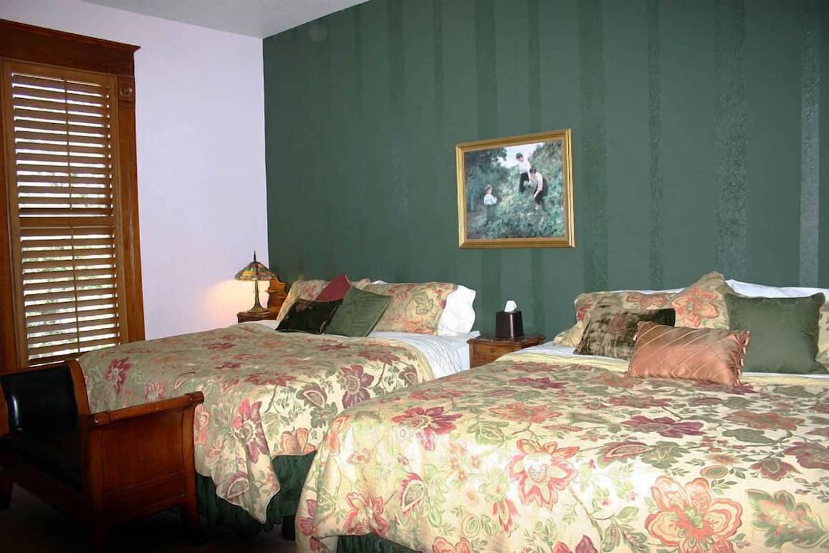 A room with two beds, a chair, a lamp, and a framed picture on the wall.