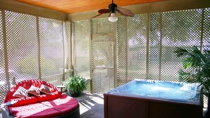A covered outdoor area with a hot tub, a cushioned seating area, and a ceiling fan.