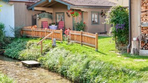 A rustic house with a wooden deck, a small garden, and a river. - Ferienwohnung 2 für 2 Personen mit Balkon, 49 m² (Inzell)