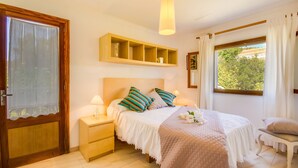 Un dormitorio con cama, mesitas de noche, ventana con cortinas y estante de madera sobre la cama.