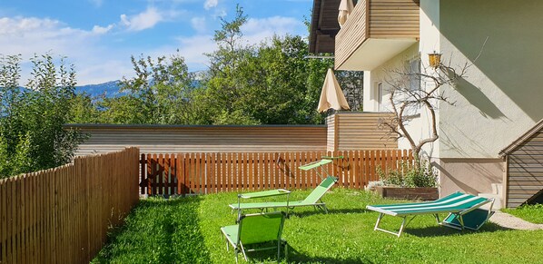 Ein Garten mit Holzzaun, Rasen und zwei grünen Liegestühlen.