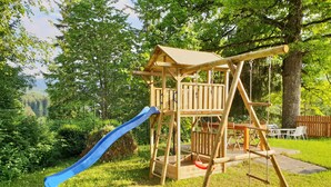 Eine Spielplatzkonstruktion aus Holz mit Rutsche und Schaukeln in einer grünen Wiese.