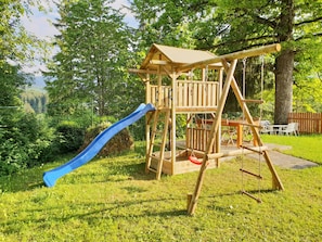 Explore the lush outdoor play area featuring a slide, swing set, and cozy bench.