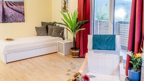 Ein Schlafzimmer mit Bett, Nachttisch, Topfpflanze und Stuhl mit Handtuch.