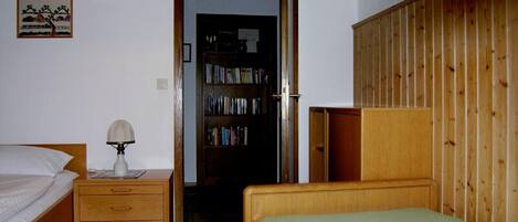 Een slaapkamer met een bed, een nachtkastje met een lamp, een houten garderobe en een boekenplank.