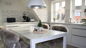 A modern kitchen with white cabinetry, a white dining table, and a large window. - Vacation apartment "Strandrose" on the Baltic Sea, free WLAN, beach chair - SEASIDE - (Rosenhagen)