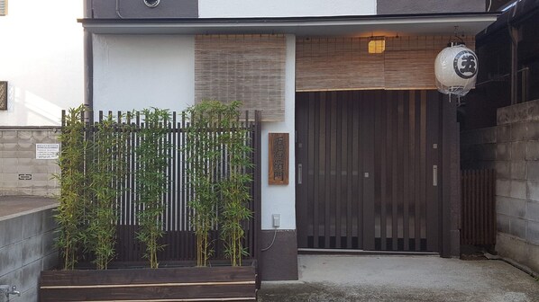 A modern building entrance with a metal gate, bamboo plants, and a wooden sign. - Goemon Fushimi (Kyoto)
