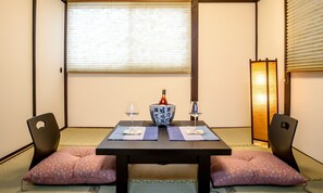 A traditional Japanese room with tatami flooring, a low table with two cushions, a bottle of sake, and two glasses. - Goemon Fushimi (Kyoto)